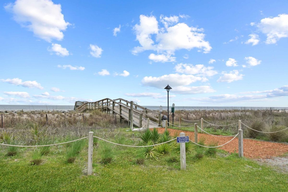 A wooden boardwalk leading to a beach with a wooden fence and a sign indicating a nature trail.