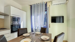 Une cuisine moderne avec une table à manger pour quatre personnes, un téléviseur fixé au mur et une fenêtre avec des rideaux.
