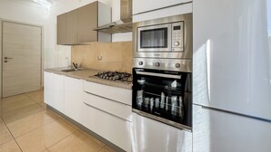 Une cuisine moderne avec des armoires blanches, un four à micro-ondes encastré, une cuisinière à gaz et un four en acier inoxydable.