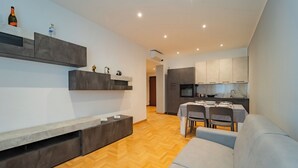 A modern living room with a grey sofa, a wooden herringbone floor, and built-in shelves with decorative items. - Dimora Bassignano - Two Bedroom Apartment, Sleeps 5 (Cuneo)