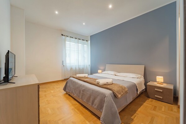 A bedroom with a bed, bedside tables, a TV, and a window with curtains.