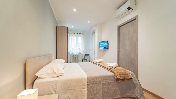 A modern hotel room with a large bed, a bedside lamp, a TV on the wall, and a radiator. - Dimora Bassignano - Two Bedroom Apartment, Sleeps 5 (Cuneo)