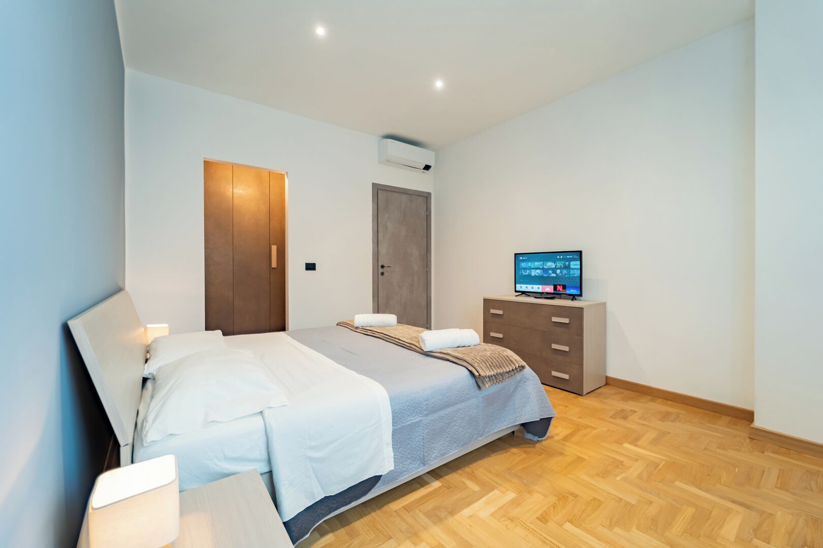 Une chambre d’hôtel moderne équipée d’un lit, d’une commode, d’un téléviseur et d’une porte.