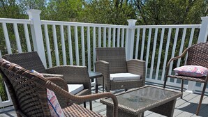 Terraza con mobiliario de mimbre, incluyendo sillas y una mesa, rodeada por una barandilla blanca.