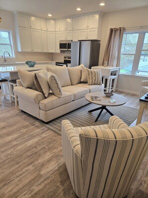 Ein modernes Wohnzimmer mit einem beigefarbenen Sofa, einem gestreiften Sessel und einem runden Couchtisch.