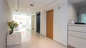 Een moderne hotel lobby met een receptiebalie, een houten deur en een potplant.