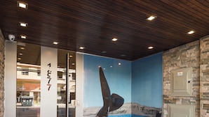 Een hotelentree met een houten plafond, een glazen deur met een nummer, een metalen leuning en een muurschildering van een boot op het water.