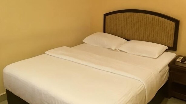 A neatly made bed with white linens, a headboard with a woven pattern, and a bedside table with a lamp. - Ronghexin Hotel (Ulan)