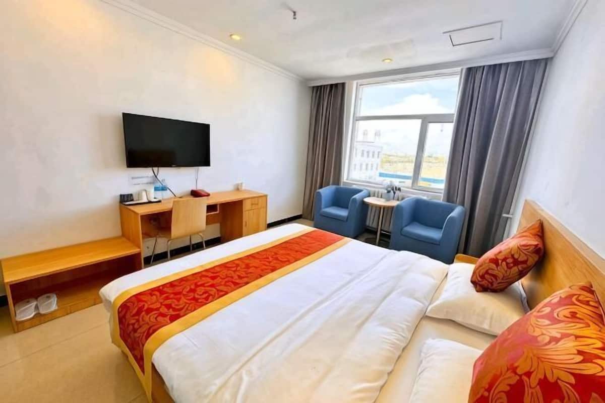 A hotel room with a bed, a desk, a chair, a television, and a window with curtains.