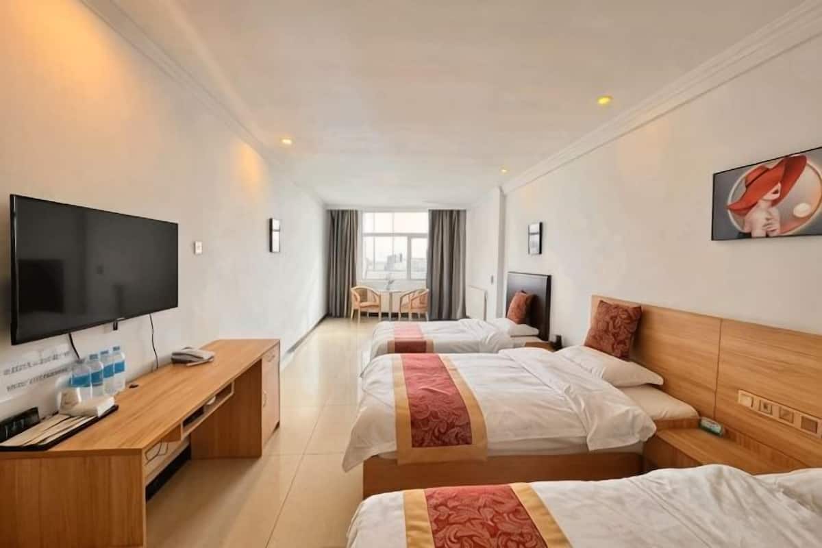 Habitación de hotel con tres camas, televisor, escritorio y ventana.