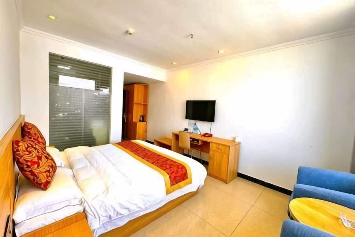 A hotel room with a bed, desk, chair, TV, and a window.
