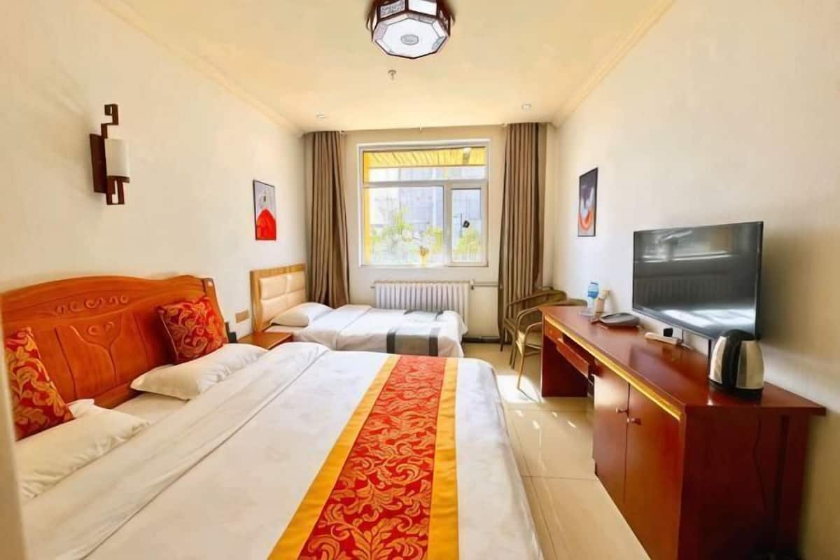 A hotel room with two beds, a television, a desk, and a window with curtains.