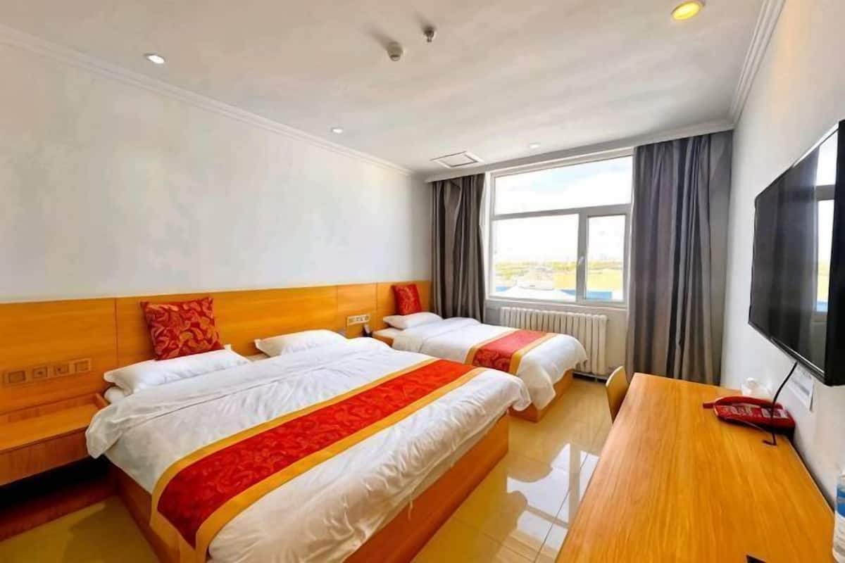 A hotel room with two beds, a wooden desk, a television, and a large window.
