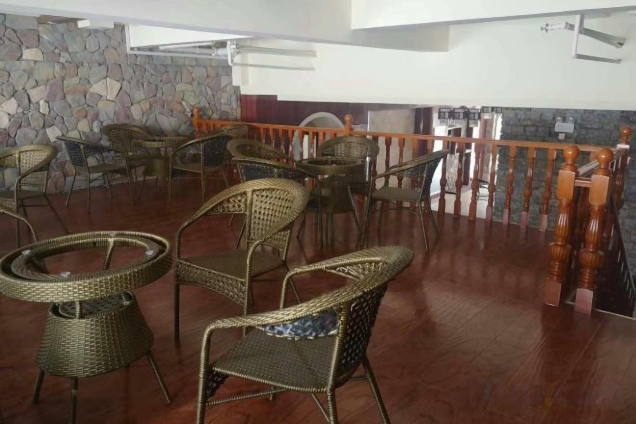 A dining area with wicker chairs and tables, a stone wall, and a wooden railing.