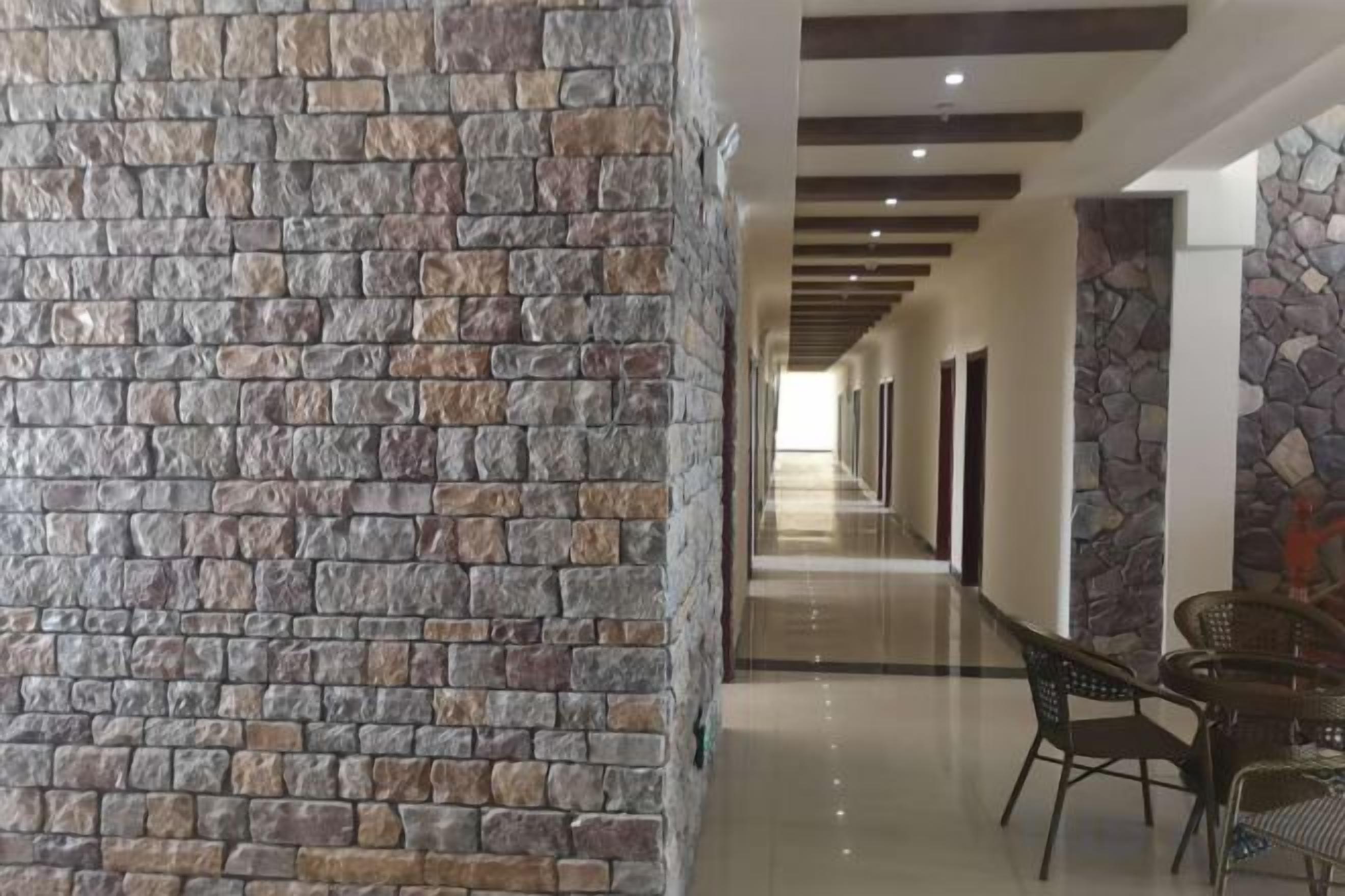 A corridor with a stone wall on one side and a seating area with chairs and tables on the other.