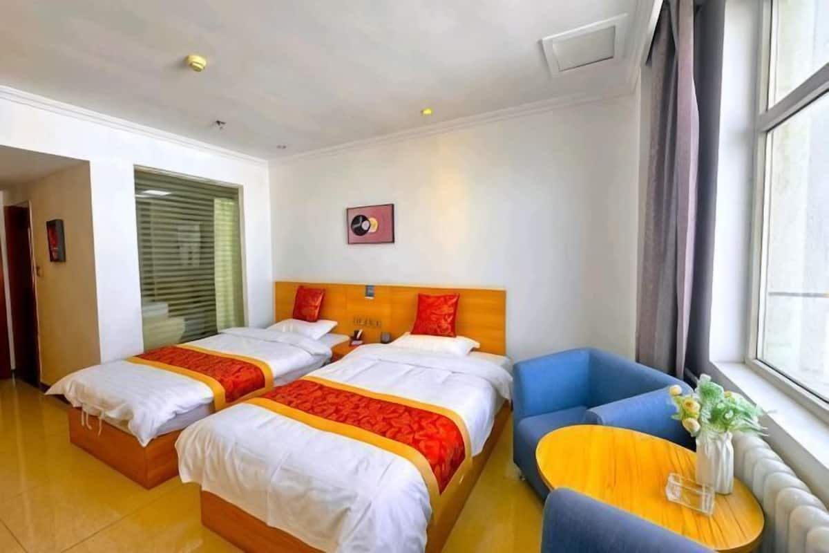 A hotel room with two beds, a sofa, a small table with a vase, and a window with curtains.