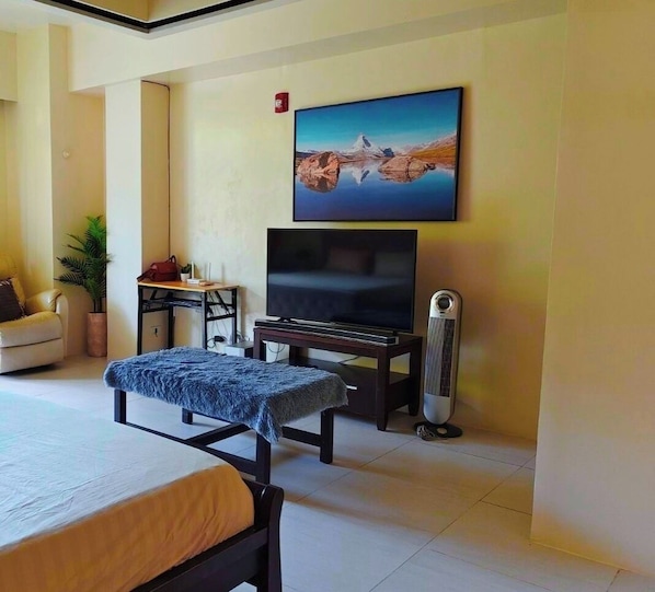 A room with a bed, a TV, a desk, a chair, a potted plant, and a wall-mounted picture. - Pico Condotel Hamilo Coast (Nasugbu)