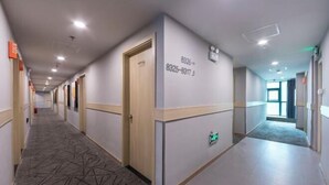 Un pasillo de hotel con piso alfombrado, puertas y una pared con números de contacto de emergencia.