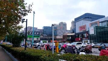 A busy urban street with modern buildings, a parking lot, and a pedestrian walkway.
