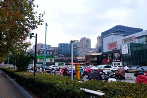 A busy urban street with modern buildings, a parking lot, and a pedestrian walkway. - Jitai Hotel (Shanghai Dahua 3rd Road Subway Station) (Shanghai)