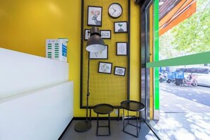 A reception area with a yellow wall, framed artwork, a clock, and a window with a view of the street. - Jitai Hotel (Shanghai Dahua 3rd Road Subway Station) (Shanghai)