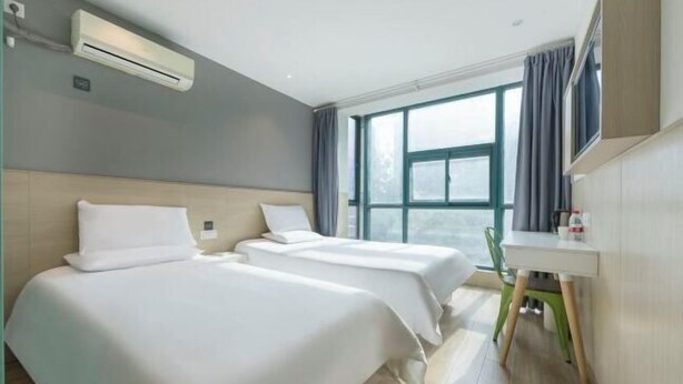 Habitación de hotel con dos camas, un escritorio, una silla, un equipo de aire acondicionado y un ventanal con cortinas.