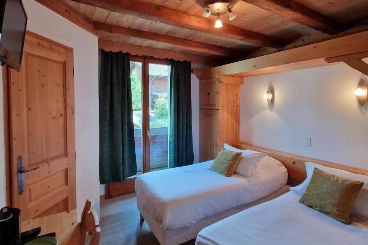 A room with two beds, wooden ceiling beams, a small table with a chair, and a television.