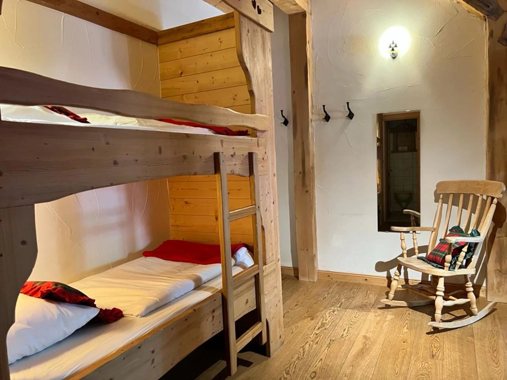 Dormitorio con literas, suelo de madera, una mecedora y un ventanal pequeño.