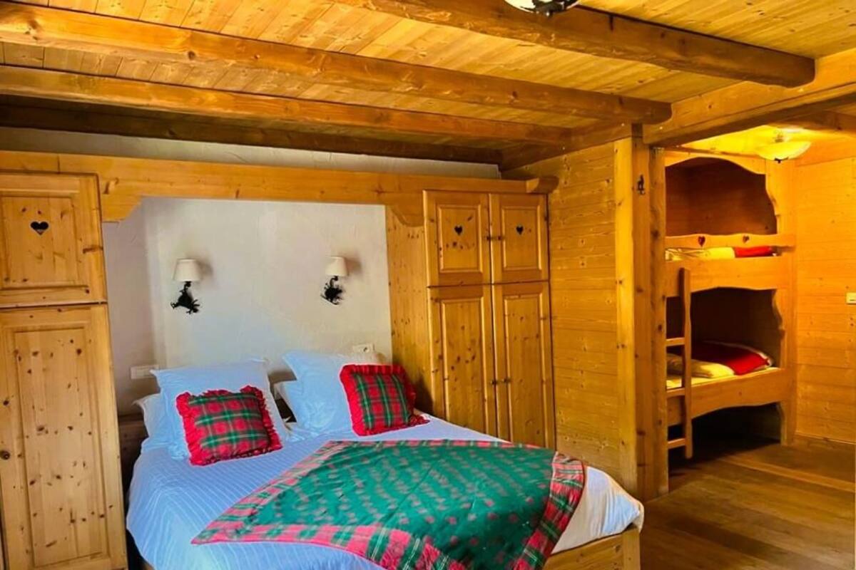 A wooden cabin bedroom with a bed, a wardrobe, and a bunk bed.