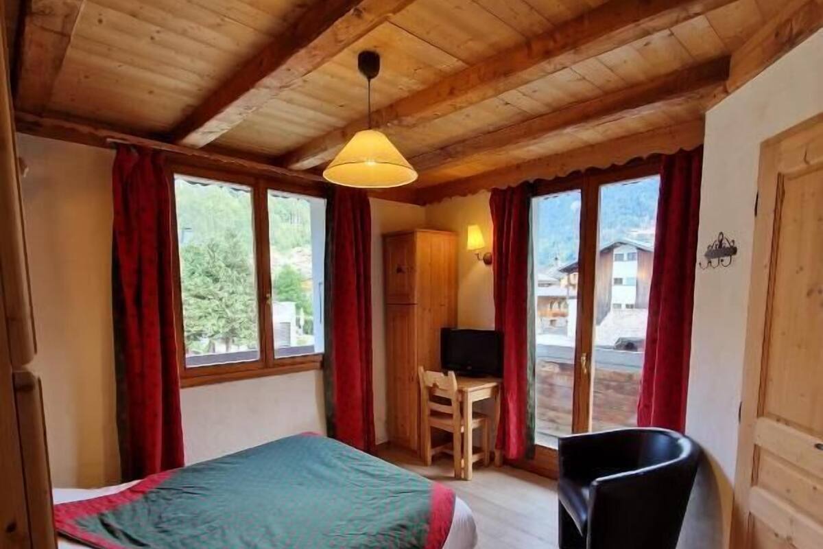 A wooden room with a bed, a desk, a chair, and a trash bin.