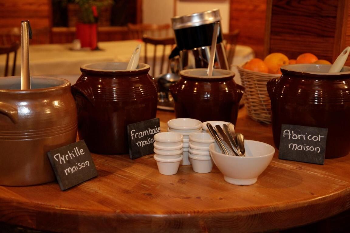 Uma mesa de madeira com diversos recipientes de cerâmica etiquetados com itens alimentares como 'Yrtille maison' e 'Abricot maison'.