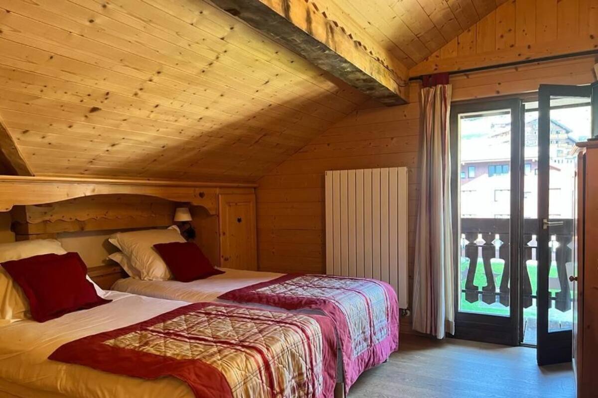 A wooden cabin bedroom with two beds, a wooden ceiling, and a sliding glass door to the outside.