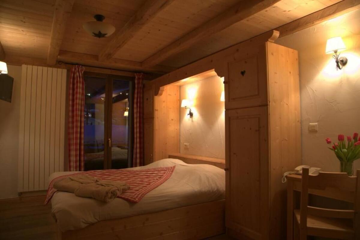A cozy wooden room with a bed, a nightstand, a lamp, and a window with curtains.