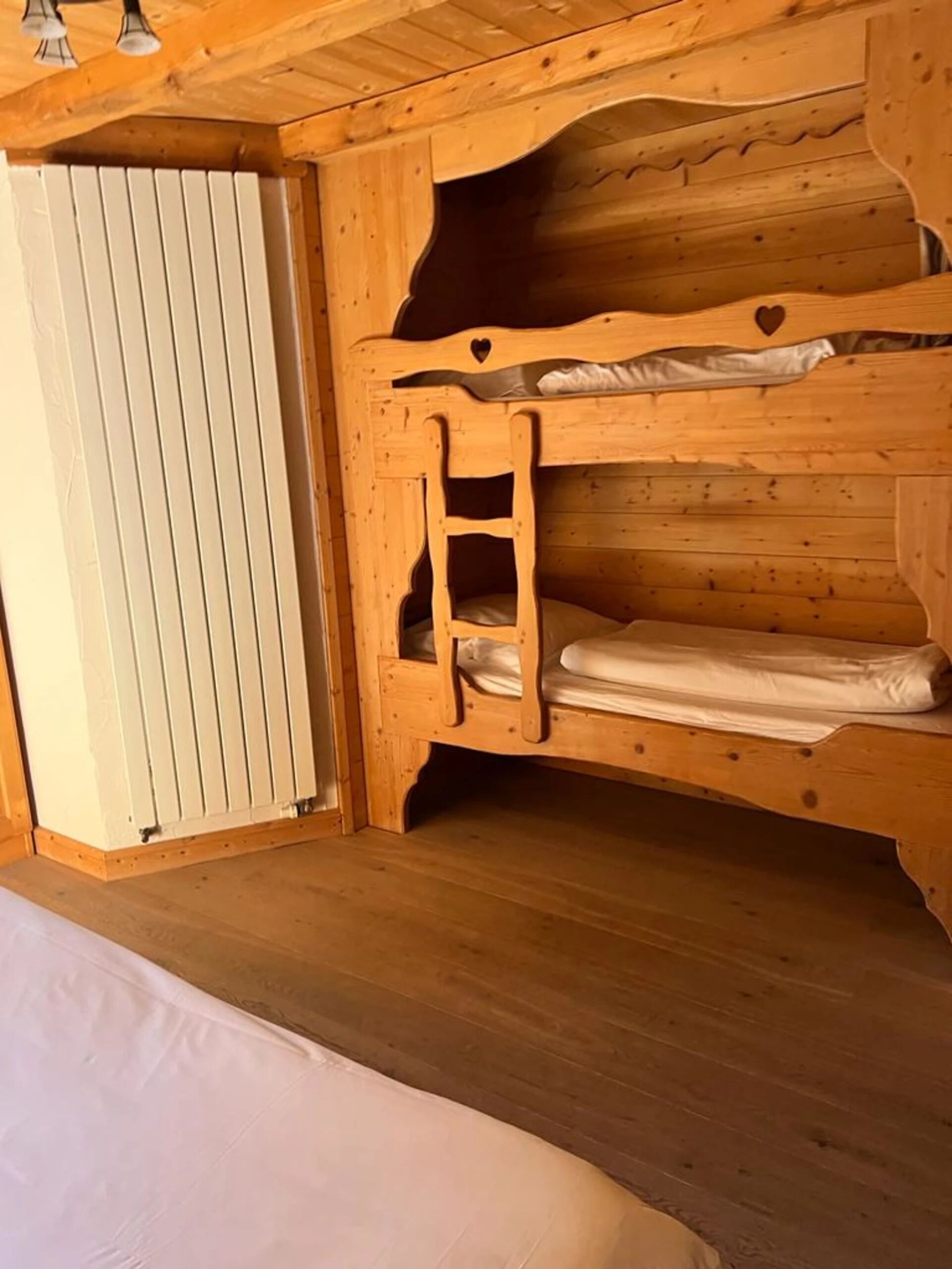 Una cama litera de madera con escalera, un radiador blanco y suelo de madera.