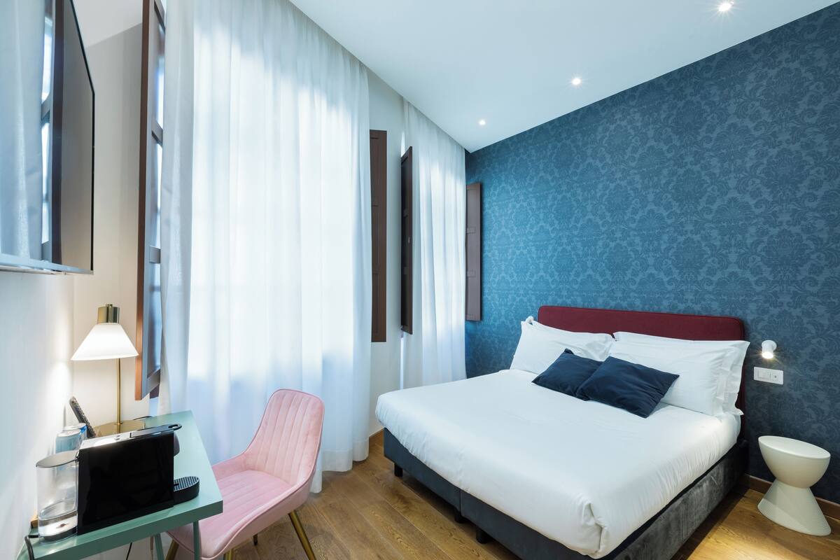 A hotel room with a bed, a desk with a lamp, a chair, and a bathroom.