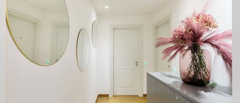 A hallway with a wooden floor, white walls, and a grey cabinet with a pink floral arrangement on top.