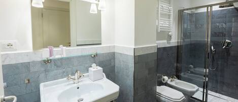 Une salle de bain moderne dotée d’un grand lavabo, de deux toilettes, d’une douche en verre et d’un miroir avec des appliques murales.
