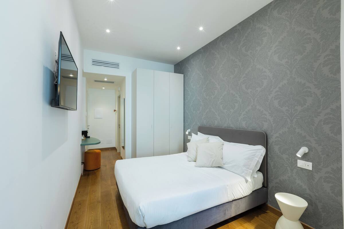 A bedroom with a bed, a bedside table, a mirror, and a toilet.