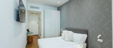 A bedroom with a bed, a bedside table, a mirror, and a toilet.