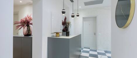 A modern hallway with a checkered floor, a reception desk, pendant lighting, and a wall-mounted clock.