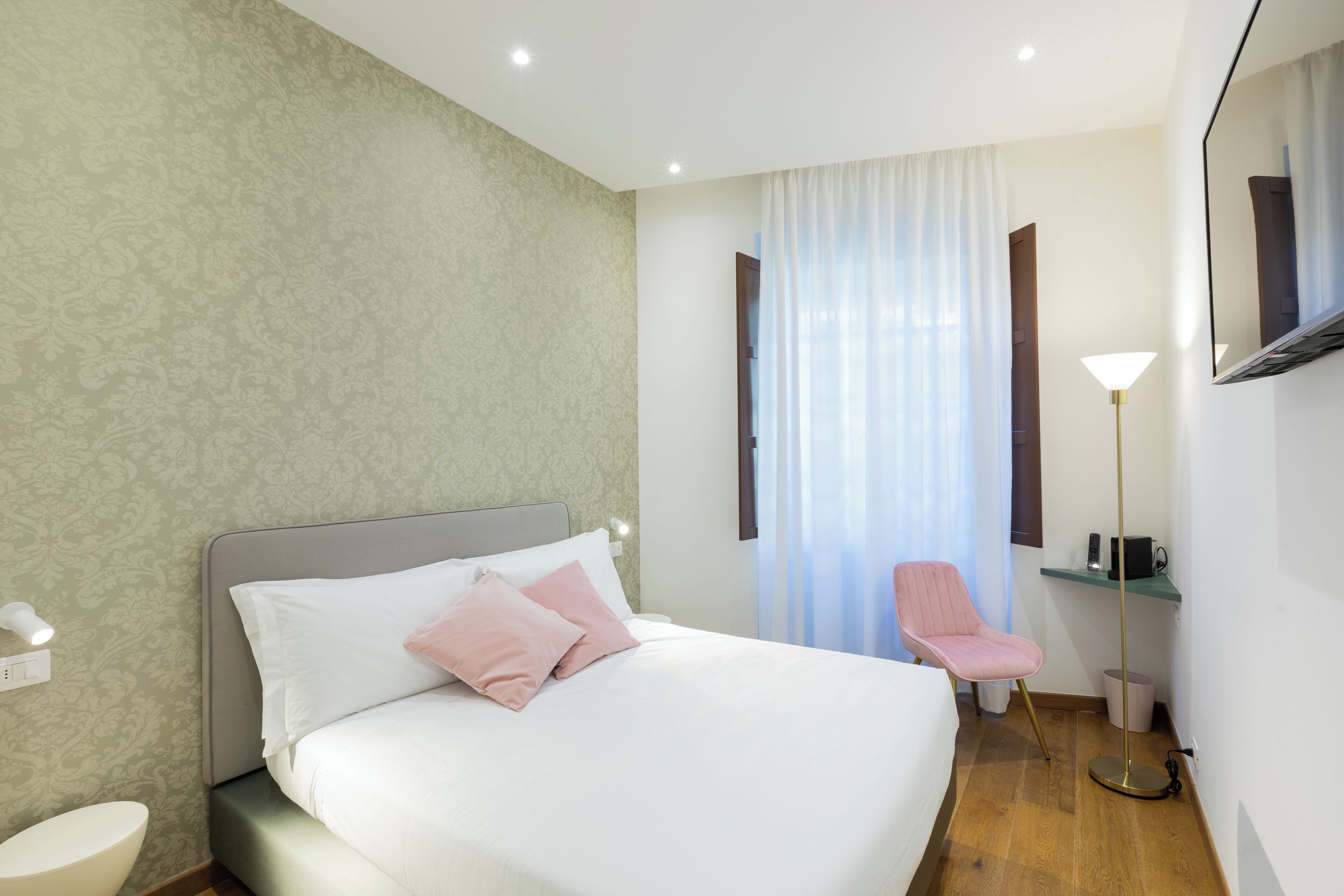A hotel room with a bed, a chair, a desk, a mirror, and a window with curtains.