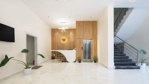 A modern hotel lobby with a reception desk, a staircase, and a large plant. - Whiteridge Premium Hotel Hitech city (Hyderabad)