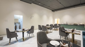 A modern dining area with round tables and grey upholstered chairs, featuring a clean, minimalist design. - Whiteridge Premium Hotel Hitech city (Hyderabad)