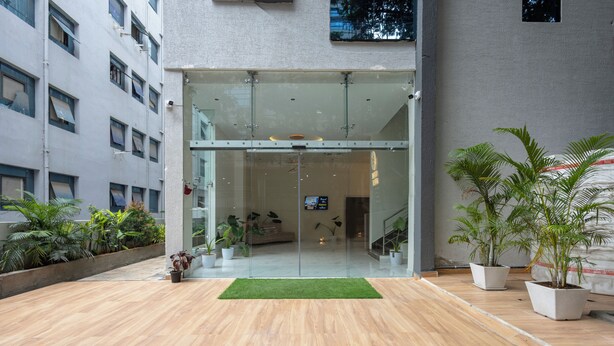 A modern building entrance with glass doors, a wooden floor, and potted plants. - Whiteridge Premium Hotel Hitech city (Hyderabad)