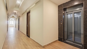A long, well-lit hallway with wooden flooring and a marble wall on one side. - Whiteridge Premium Hotel Hitech city (Hyderabad)