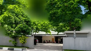 A gated entrance to a building with a covered driveway, surrounded by trees. - QUEEN CITY HOTEL (Banjarmasin)