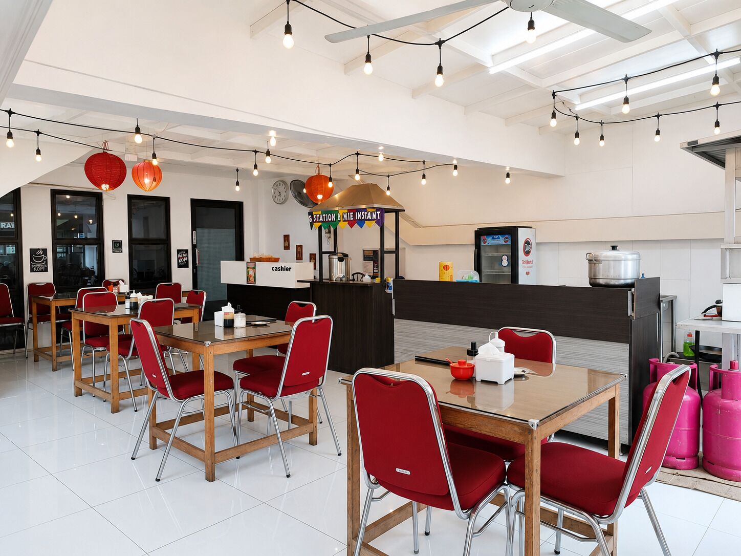 A modern restaurant with wooden tables and red chairs, a cash register, and a kitchen area in the background.