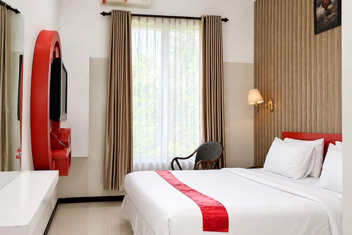 Habitación de hotel con cama, escritorio, silla, televisor y cortinas.