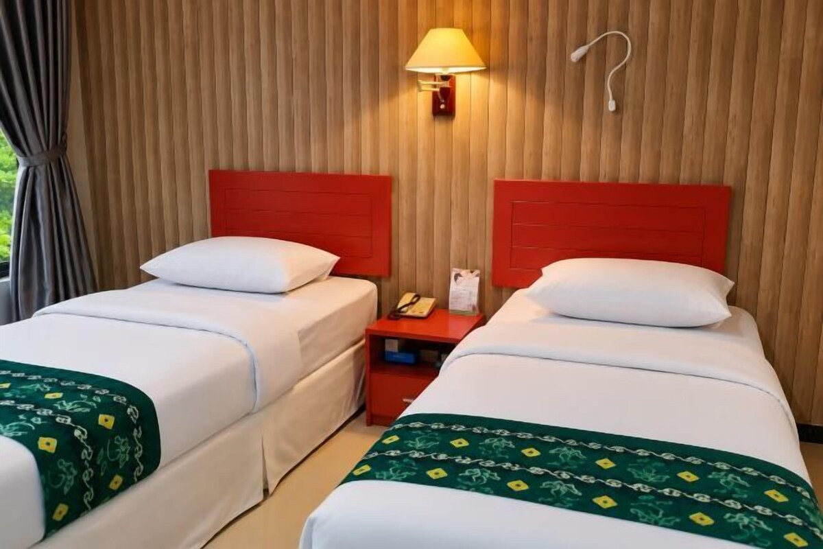 A hotel room with two beds, a nightstand with a telephone, and a wall-mounted light fixture.