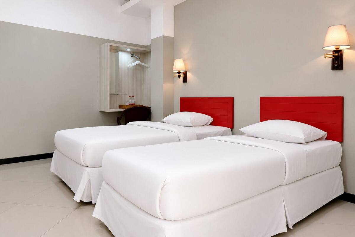 Habitación de hotel con dos camas, un espejo y dos lámparas fijadas a la pared.